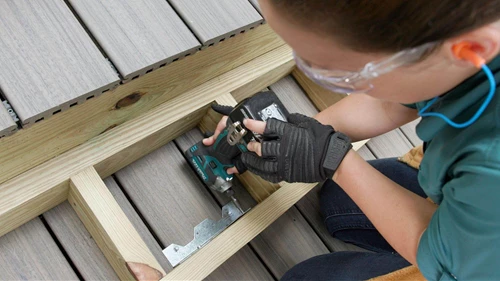 Person with a electric drill in their hand screwing in a bracket on box stairs