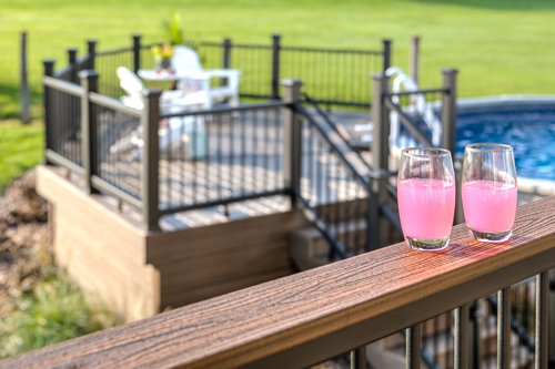 A pair of drinks resting atop a cocktail rail on an aluminum railing.