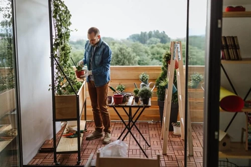 Person Watering Plant On Patio Showcasing Balcony Garden Ideas And Greenery Immersion