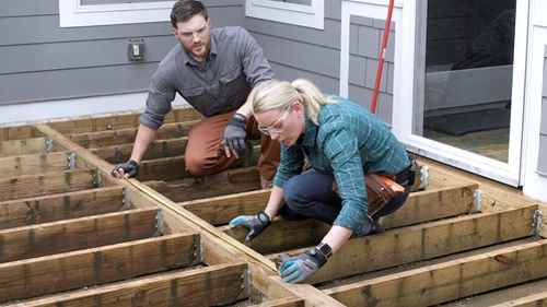 2 people measuring a deck board